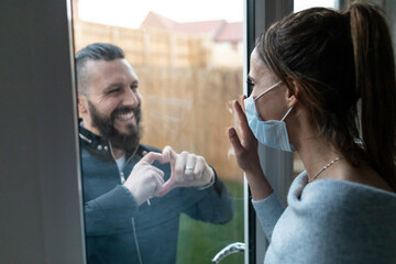 Boyfriend show heart shape gesture to girlfriend through window glass while during COVID-19 crisis