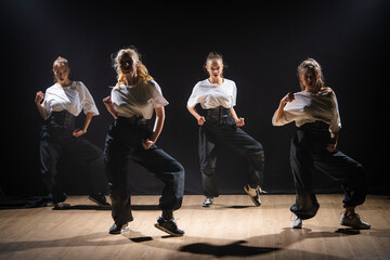 In the shot on a black background, shine the light from above dance collective, a team consisting of young girls. They demonstrate various dance moves towards jazz funk.