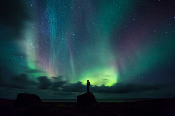 Norway, Lofoten Islands, Eggum, man standing on rock and watching northern lights - obrazy, fototapety, plakaty