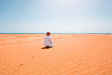Bedouin in National dress praying in the desert, rear view, Wahiba Sands, Oman