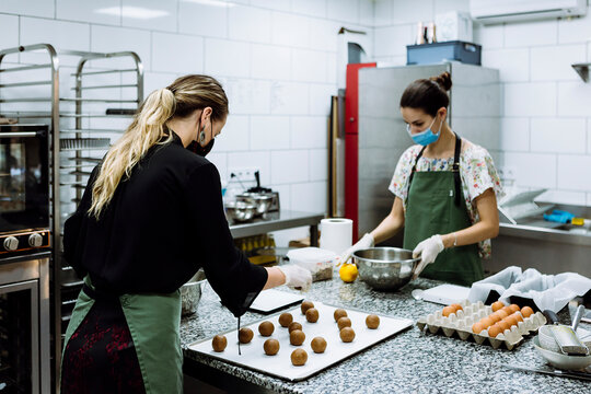 Female bakers making cookies at kitchen in bakery during COVID-19