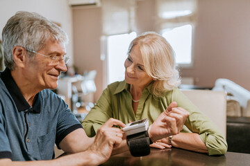 Smiling senior couple taking blood pressure - obrazy, fototapety, plakaty