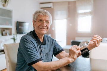 Smiling senior man taking his blood pressure - obrazy, fototapety, plakaty