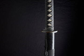 Horizontal photo of sheathed katana with details of the handle and sheath, traditional Japanese sword isolated on black background - obrazy, fototapety, plakaty