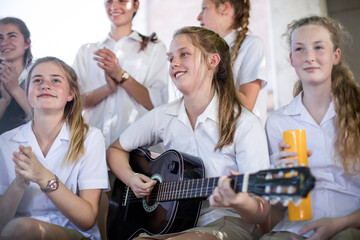 Female high school student playing guitar with group of school friends outside
