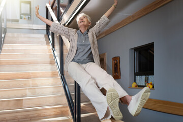 Happy senior woman sliding down a staircase