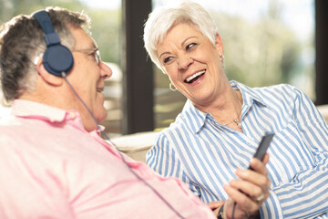 Happy senior couple with cell phone and headphones on couch at home