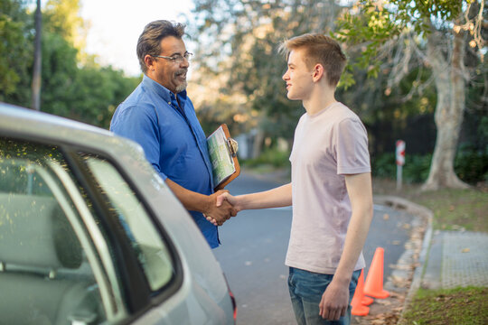 Learner driver and instructor shaking hands at car - Powered by Adobe