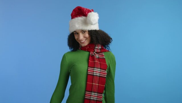 Joyful attractive curly dark-haired woman in green turtleneck, long red checkerd scarf around neck shaking head, pompom fluttering from side to side. High quality 4k footage