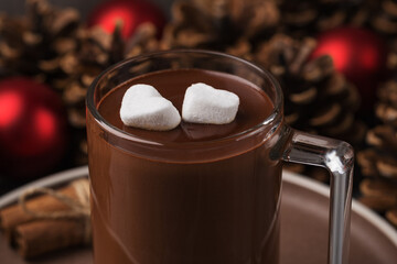 Close-up mug filled with hot chocolate with marshmallows on a dark table. Christmas and New Year's composition. Red Christmas balls, pine cones in background. Selective Focus.