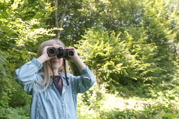 Cute little girl exploring nature looking through binoculars. Child playing outdoors. Kids travel, adventure and bird watching concept.	