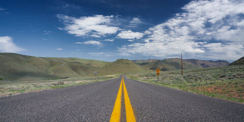 Lonely two lane road in a hilly dry desolate region centered on a double yellow line with a deep...