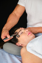 Woman getting face massage with a facial cooling metal roller. Professional skin care treatment.