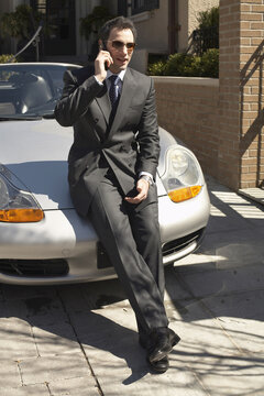 Businessman with Cellular Phone Leaning on Car