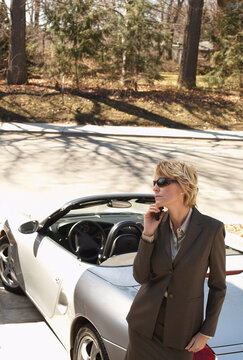 Businesswoman with Cellular Phone Leaning against Car