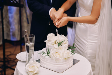Obraz na płótnie Canvas Bride and groom cut a wedding cake with a knife on a table. Cropped. Faceless