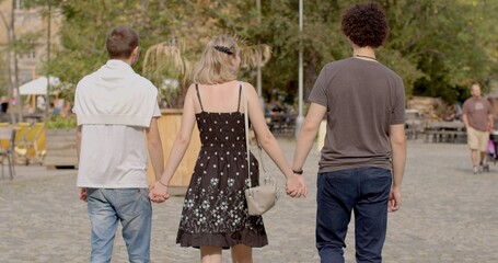 Urban environment. Romantic relationships among three individuals polyamory, involve consensually and openly loving and connecting with multiple partners simultaneously. Girl and two guys, back view. 