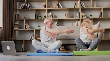Active elderly couple doing exercises and watching online exercise tutorials on laptop in living room at home.
