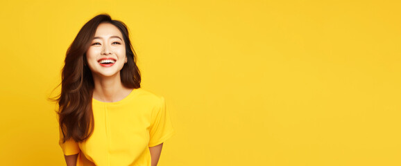 Beautiful Asian woman with long wavy hair and wearing yellow t-shirt smiling on yellow background