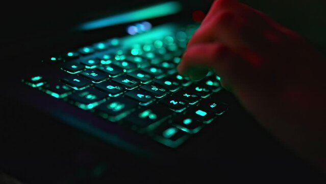 Close up view of unrecognizable person's hand playing video game on a laptop with a black keyboard with multicolored neon backlit. Focus on WSAD, SHIFT keys.