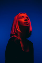 A striking portrait of a woman bathed in contrasting blue and red lights, exuding a sense of...