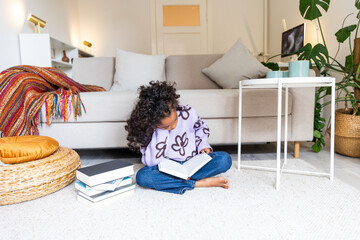 POC girl sitting on carpet infront of sofa reading a book