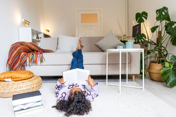POC child lying on carpet in front of sofa ready a book