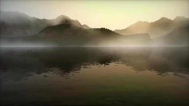 tranquil lake covered in morning mist, with a range of mountains in the background. A faint light illuminates the contours of the mountains through the mist, creating a mystical and serene atmosphere.
