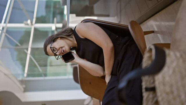 Casual chat, confident and beautiful hispanic woman with glasses happily speaking on the phone at a modern hotel hall lounge