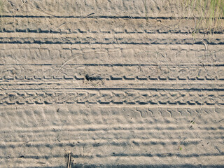 Beige sand with many traces of bicycle treads in the rays of the setting sun. Background with...