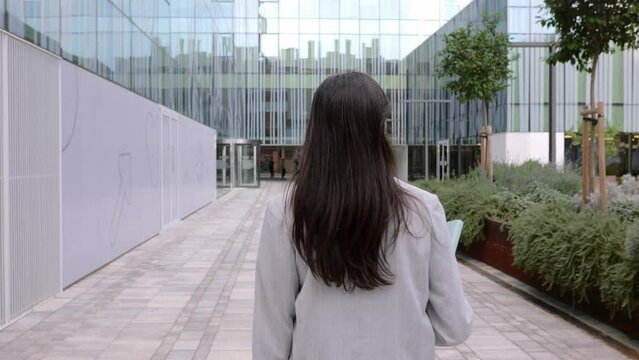 Rear view of young adult business woman walking in a co-working office area. Professional confident empowered female entrepreneur going to work at the office.