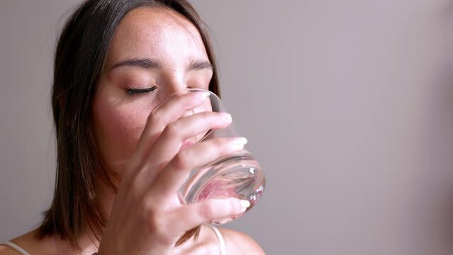 Young woman drinking glass of mineral water in the morning at home. Healthy lifestyle and well-being concept.