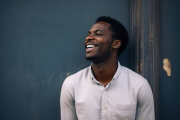 Black man laughing in a light shirt against a dark textured wall