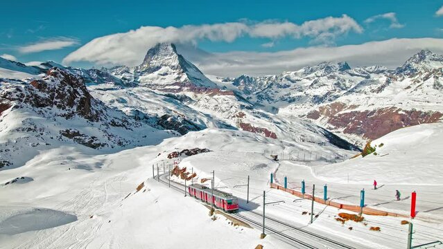 View from above of a passenger red train in the Matterhorn Alps in Europe, Switzerland. Aerial close-up view of a Swiss train with tourists on a railway and Matterhorn mountain in the background. 
