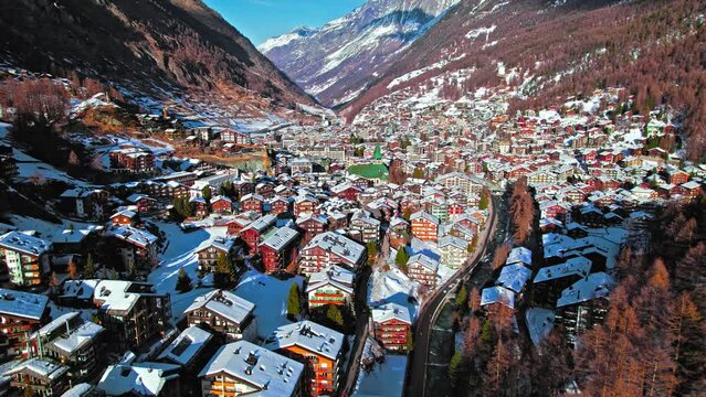 Aerial view of wooden Swiss houses and a Cathedral covered by snow in Zermatt. Ski Resort Town with typical Swiss buildings on hills with picturesque rivers in the Alps, Zermatt, Europe.