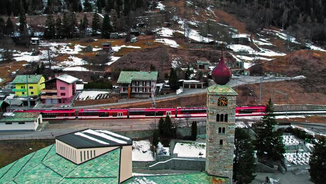 Aerial view of the Swiss clock tower and passenger train ride in a cold winter ambience, Switzerland. Typical colourful houses covered by snow in the Alps, Europe.