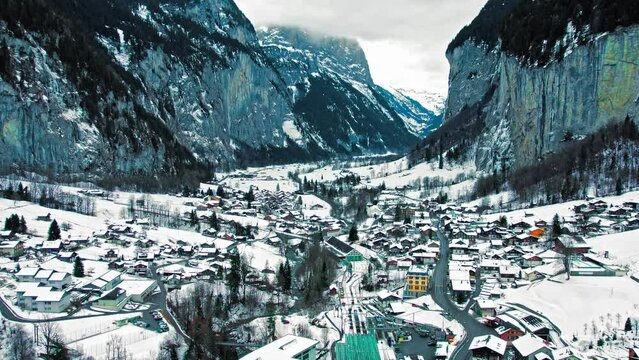 Scenic view from above of Lauterbrunnen houses in the Swiss Alps covered by snow. Aerial view of the valley featuring rocky cliffs and falls during winter in Switzerland.