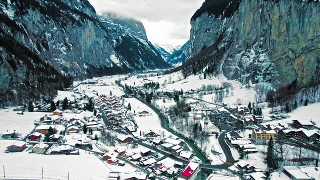 Scenic view from above of Lauterbrunnen houses in the Swiss Alps covered by snow. Aerial view of the valley featuring rocky cliffs and falls during winter in Switzerland.