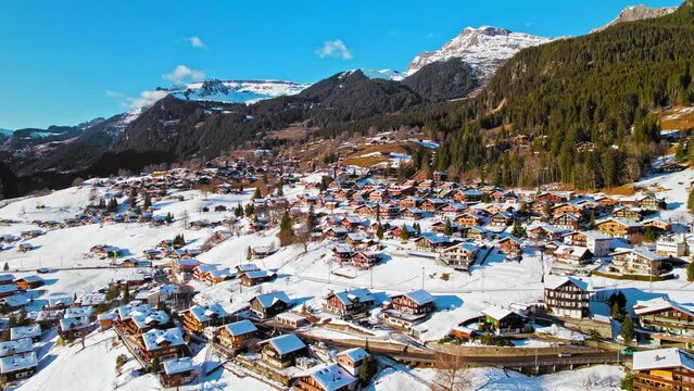 Cinematic view from above of colourful wooden houses and the Bernese Alps in Grindelwald. Panoramic aerial view of Swiss glacier village and unique Alpine landscape covered by snow in Switzerland.