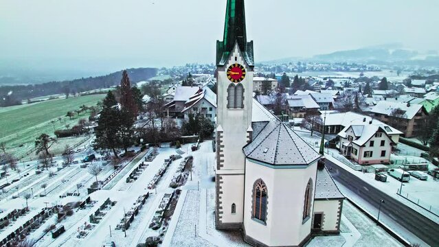 Drone view of snow falling over a church in Switzerland. Aerial view of a typical traditional Tower clock in Europe during winter.