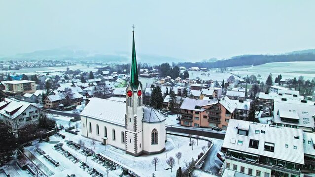 Drone view of snow falling over a church in Switzerland. Aerial view of a typical traditional Tower clock in Europe during winter.