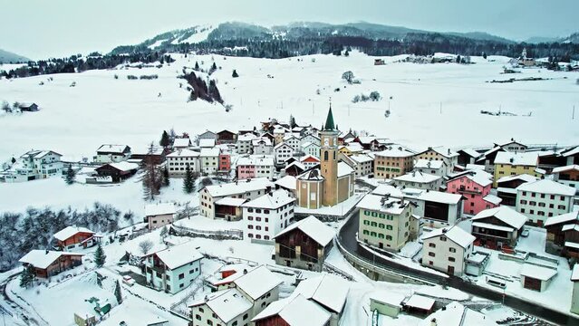 Aerial panoramic view of colourful houses and churches in Surses, Switzerland. Drone view of Houses covered with snow in the middle of the Swiss Alps during winter.