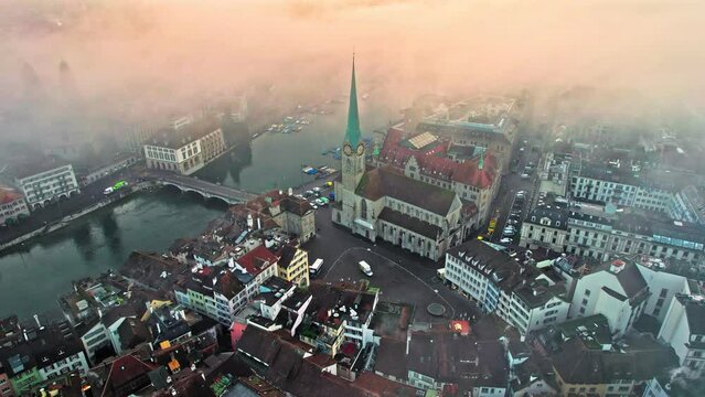 Aerial foggy view of Grossm&uuml;nster and Fraum&uuml;nster Church in Zurich. Cinematic view of the turquoise lake and bridge, colourful houses and high tower in Switzerland.