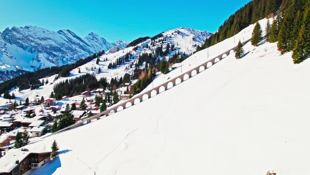 Aerial view of a village with colourful houses and an electric train taking tourists to a car-free resort in Murren. View of Alpine Swiss mountain covered with snow in winter at Lauterbrunnen Valley.