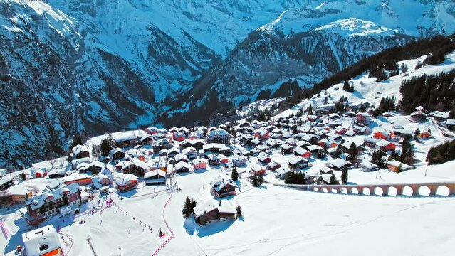 Aerial view of a village with colourful houses and an electric train taking tourists to a car-free resort in Murren. View of Alpine Swiss mountain covered with snow in winter at Lauterbrunnen Valley.