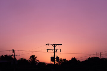 Silhouette of high voltage electric pole at sunset sky background.