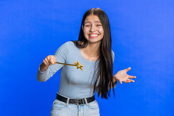 Magician witch young woman gesturing with magic wand fairy stick, making wish come true, casting magician spell, advertising holidays sale discount. Smiling girl isolated on blue studio background