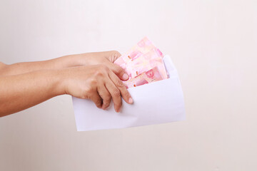 Hands holding envelope with indonesia banknotes on white background. Woman hand takes out money from an envelope, close-up. Bribe corruption, salary, earning and savings concept