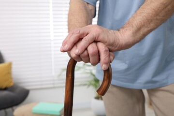 Senior man with walking cane at home, closeup. Space for text
