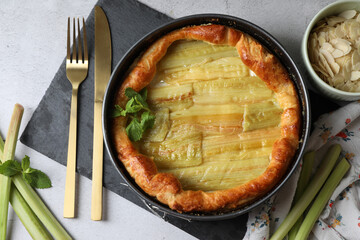 Freshly baked rhubarb pie, stalks and cutlery on light grey table, flat lay